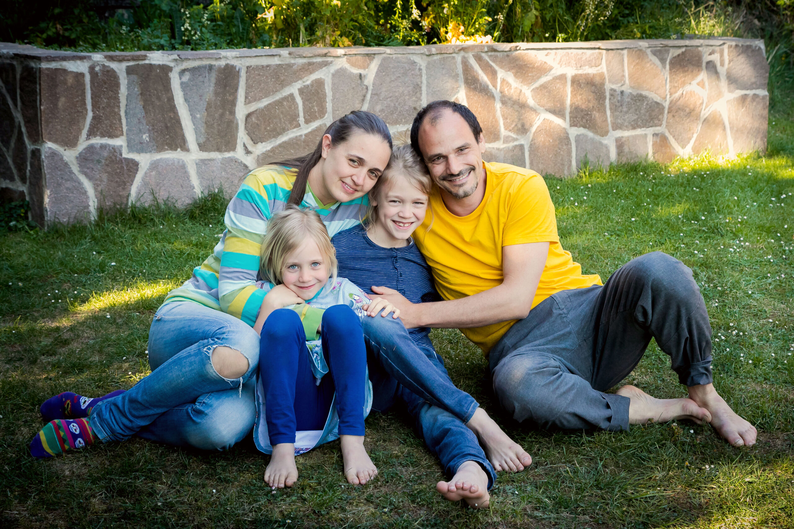 Familie mit Vater, Mutter und zwei Kinder sitzt lächelnd auf dem Rasen im Garten