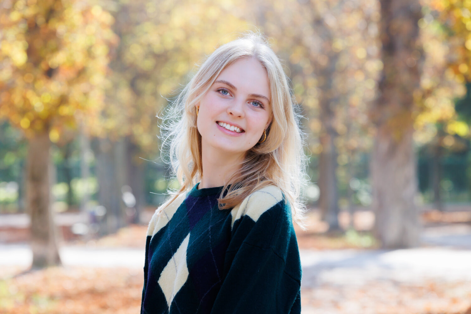 Porträt einer lächelnden jungen Frau mit blondem Haar im herbstlichen Park